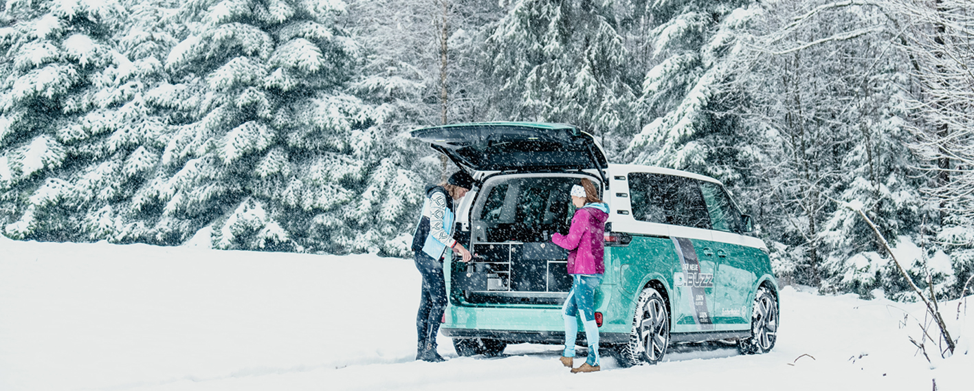 VW Bus mit Campingbox im Heck des Vans im Schnee mit zwei Frauen